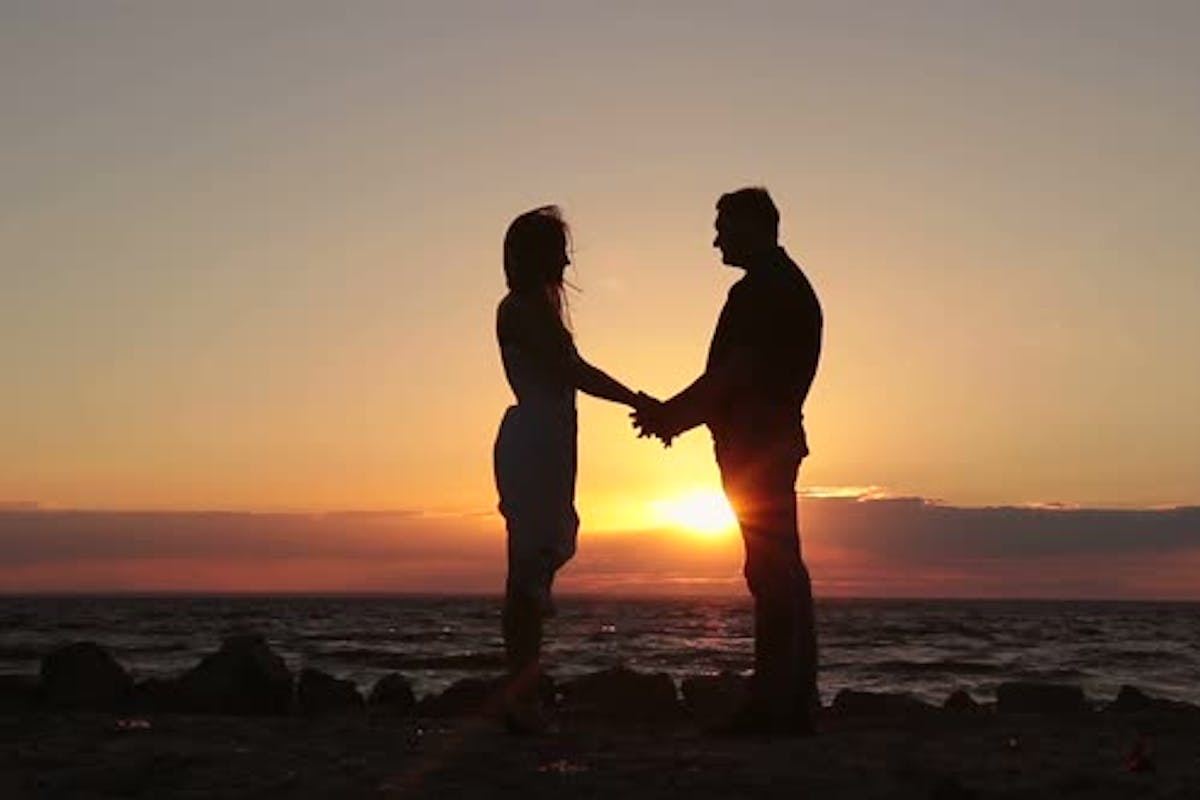 Happy couple holding hands on beach sunset